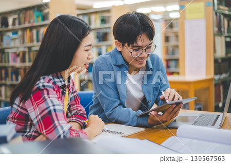Students are consulting each other working on laptops and searching for books to study, make reports, find useful information in university room. Concept of reading, learning and intelligence. 139567563