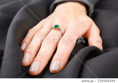 Beautiful female hand with gold ring with diamonds and emerald on gray background Beautiful female hand with gold ring with diamonds and emerald on gray background 139568349