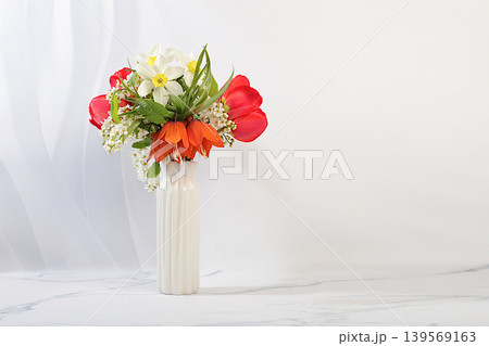 Still life with beautiful spring branches of blooming bird cherry, tulips, daffodils, and a fritillary in a vase against an elegant background. Abstract floral arrangement and banner for the screen. Still life with beautiful spring branches of blooming bird cherry, tulips, daffodils, and a fritillary in a vase against an elegant background. Abstract floral arrangement and banner for the screen. 139569163