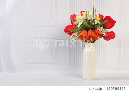 Still life with beautiful spring branches of blooming bird cherry, tulips, daffodils, and a fritillary in a vase against an elegant background. Abstract floral arrangement Still life with beautiful spring branches of blooming bird cherry, tulips, daffodils, and a fritillary in a vase against an elegant background. Abstract floral arrangement 139569165