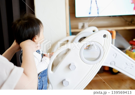 親に着替えさせてもらう1歳児の後ろ姿。 親に着替えさせてもらう1歳児の後ろ姿。 139569413