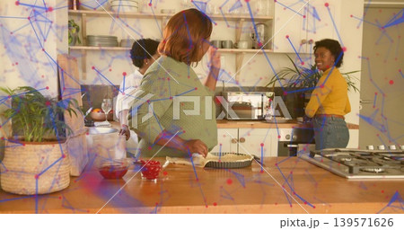 Holding white cloth, center woman wearing green knit prepping pie at kitchen island with cherries Holding white cloth, center woman wearing green knit prepping pie at kitchen island with cherries 139571626