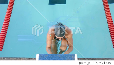 Preparing female swimmer bracing block in pool amid red ropes wearing dark swimsuit cap and goggle Preparing female swimmer bracing block in pool amid red ropes wearing dark swimsuit cap and goggle 139571739