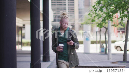 Walking man glancing at phone while holding coffee in plaza, wearing green hoodie with backpack Walking man glancing at phone while holding coffee in plaza, wearing green hoodie with backpack 139571834