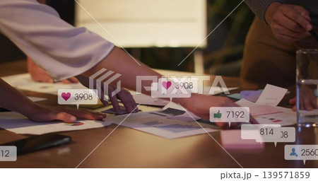 Pointing colleagues leaning over wooden table, reviewing charts with social overlays, satin top Pointing colleagues leaning over wooden table, reviewing charts with social overlays, satin top 139571859