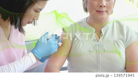 Giving nurse vaccinating Asian woman in clinic with syringe, nitrile gloves, scrubs, green overlay Giving nurse vaccinating Asian woman in clinic with syringe, nitrile gloves, scrubs, green overlay 139571945