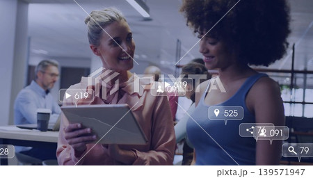 Smiling two women holding cracked tablet viewing social overlays in office, pink blouse blue top Smiling two women holding cracked tablet viewing social overlays in office, pink blouse blue top 139571947