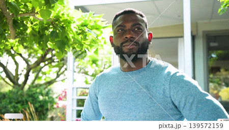 Standing man with trimmed beard gazing upward on front porch, wearing light blue knit sweater Standing man with trimmed beard gazing upward on front porch, wearing light blue knit sweater 139572159
