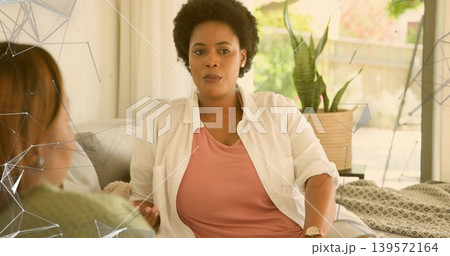Talking woman in rose-pink top and open shirt in living room, showing geometric overlays and plant Talking woman in rose-pink top and open shirt in living room, showing geometric overlays and plant 139572164