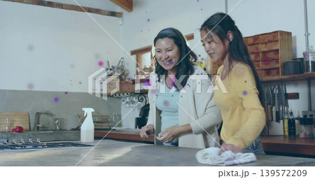 Wiping daughter in yellow top, mother in cardigan at kitchen island, with sprayer and cloth Wiping daughter in yellow top, mother in cardigan at kitchen island, with sprayer and cloth 139572209