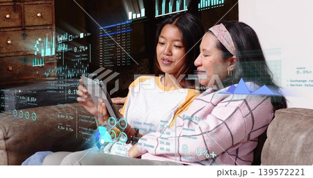 Discussing daughter holding tablet and mother leaning in on brown sofa, viewing AR data charts 139572221