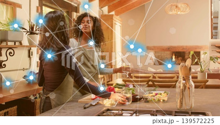 Two women wearing aprons preparing salad on cutting board, pouring drinks in home kitchen, overlay Two women wearing aprons preparing salad on cutting board, pouring drinks in home kitchen, overlay 139572225