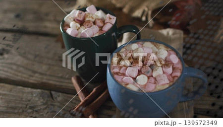 Sitting blue green mugs steaming cocoa on wooden table, with pink marshmallows and cinnamon sticks 139572349