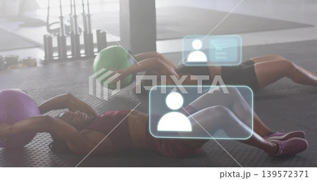 Crunching partners wearing sportswear on gym mat, holding green purple medicine balls with HUD Crunching partners wearing sportswear on gym mat, holding green purple medicine balls with HUD 139572371