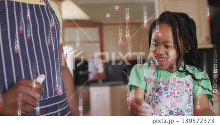 Smiling girl in apron mixing flour in kitchen, adult in striped apron holding cloth, binary overlay 139572373