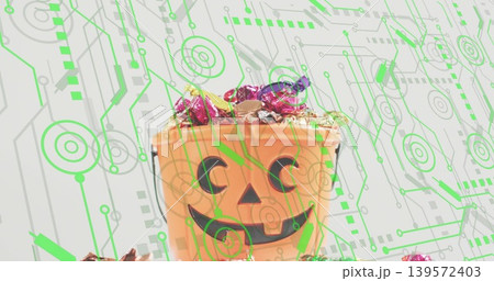 Sitting orange jack-o'-lantern bucket holding foil candies, tinsel on pale table with neon circuit 139572403