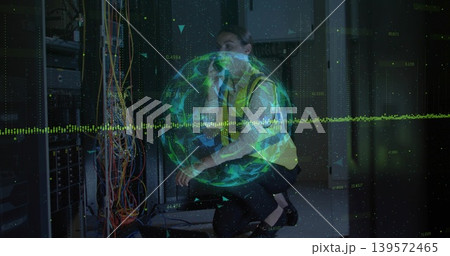 Kneeling mid-adult female tech routing multicolor cables at rack in hi-vis vest with green hologram 139572465