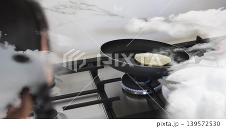 Cooking woman in dark top leaning over gas stove at home, flipping pancake with spatula Cooking woman in dark top leaning over gas stove at home, flipping pancake with spatula 139572530