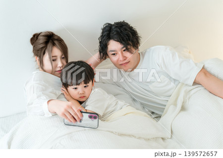 ベッドルームで男の子をスマホを使って寝かしつける夫婦 139572657