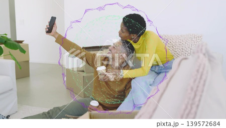 Smiling couple posing for phone selfie in living room, woman in yellow top, boxes, AR overlay Smiling couple posing for phone selfie in living room, woman in yellow top, boxes, AR overlay 139572684
