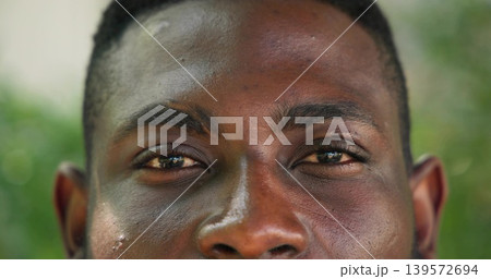 Gazing African American man filling frame outdoors, showing skin texture and green bokeh 139572694