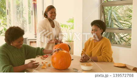 Scooping three mid adult women wearing sweaters carving pumpkins in bright kitchen, with seeds Scooping three mid adult women wearing sweaters carving pumpkins in bright kitchen, with seeds 139572708