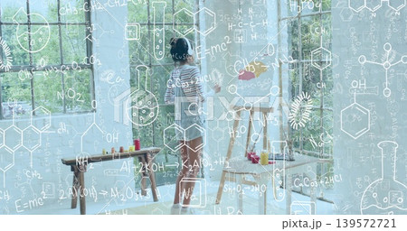 Painting artist in striped-shirt denim-dress at easel in studio with paints and formula overlay Painting artist in striped-shirt denim-dress at easel in studio with paints and formula overlay 139572721