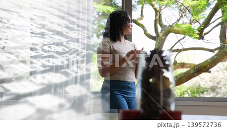 Holding ceramic mug, woman with curly hair gazing out large window with sheer curtain, copy space Holding ceramic mug, woman with curly hair gazing out large window with sheer curtain, copy space 139572736