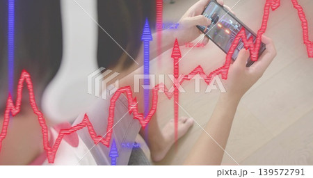 Sitting Asian man in white top gray shorts on floor holding phone with headphones, finance overlays 139572791