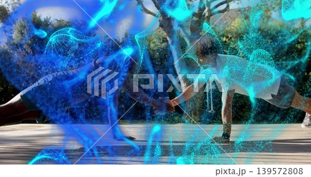 Doing partnered plank, pair in tank tops clasping hands on wooden backyard deck, blue overlay 139572808