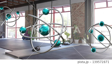 Hanging large orbital sculpture catching window light in warehouse studio, showing suspension ropes Hanging large orbital sculpture catching window light in warehouse studio, showing suspension ropes 139572871