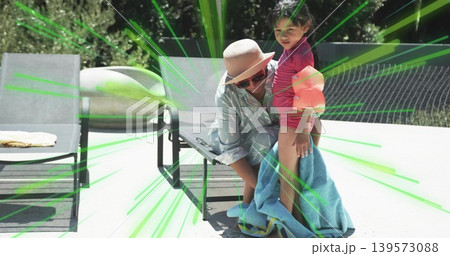 Kneeling adult woman adjusting blue towel around child at poolside patio, with sun hat, floaties Kneeling adult woman adjusting blue towel around child at poolside patio, with sun hat, floaties 139573088