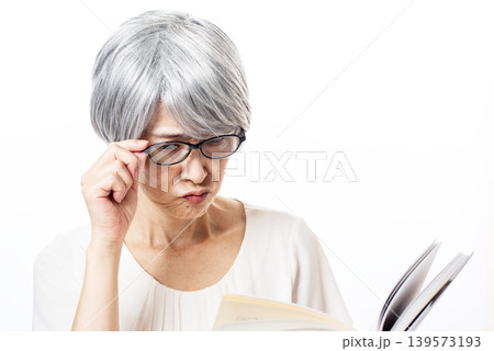 黒ぶちの老眼鏡をかけて苦労して読書をするシニア女性 139573193