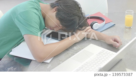 Napping Asian man in green tee leaning on glass table at home, with laptop, phone, headset Napping Asian man in green tee leaning on glass table at home, with laptop, phone, headset 139573387
