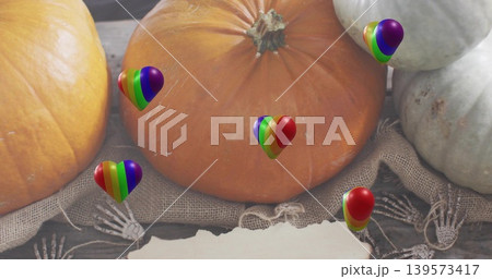 Showing large orange pumpkin resting on burlap on wood, with rainbow-heart balloons, skeleton hands Showing large orange pumpkin resting on burlap on wood, with rainbow-heart balloons, skeleton hands 139573417