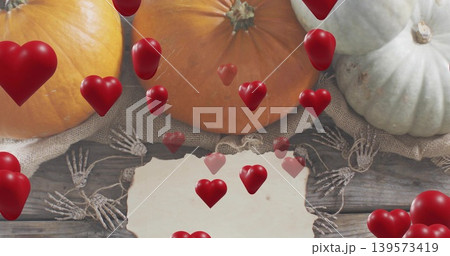Showing three pumpkins sitting on burlap on wood planks with paper bone garland floating red hearts 139573419