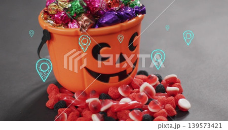 Showing pumpkin bucket holding foil candies on dark tabletop, red gummies and turquoise pins Showing pumpkin bucket holding foil candies on dark tabletop, red gummies and turquoise pins 139573421