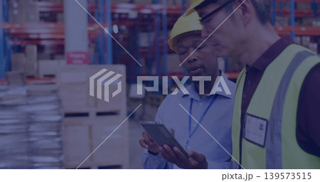 Holding tablet, two workers inspecting inventory in aisle, wearing hard hats and hi-vis vest 139573515