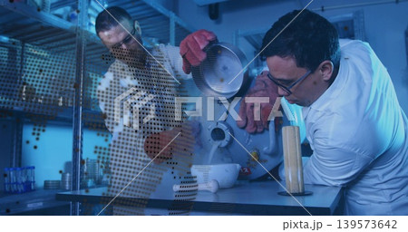 Leaning lab-coated man steadying bowl receiving Dewar vapor at lab bench, red gloves, copy space Leaning lab-coated man steadying bowl receiving Dewar vapor at lab bench, red gloves, copy space 139573642