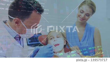 Examining dentist leaning over child in dental clinic, using mirror, blue gloves and market charts 139573717