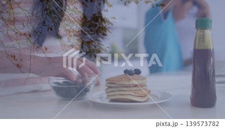 Showing pancake stack with blueberries on kitchen counter, adult reaching into bowl, branch overlay Showing pancake stack with blueberries on kitchen counter, adult reaching into bowl, branch overlay 139573782