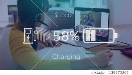 Writing girl in yellow top headset leaning at home table, laptop showing call 58% charging overlay Writing girl in yellow top headset leaning at home table, laptop showing call 58% charging overlay 139573865