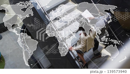 Riding peers holding rail, file wearing suit and blazer ascending atrium escalator with map overlay 139573940