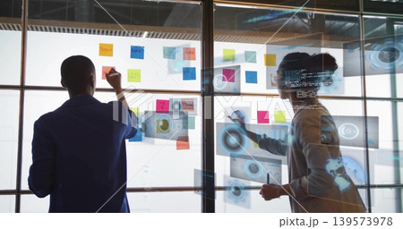 Writing women colleagues in jackets sketching on glass partition at office, with sticky notes, code Writing women colleagues in jackets sketching on glass partition at office, with sticky notes, code 139573978