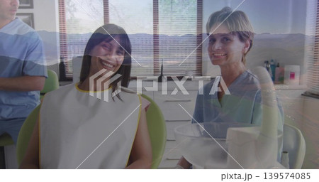 Smiling patient in white bib yellow trim, sitting in green dental chair, staff in blue scrubs 139574085