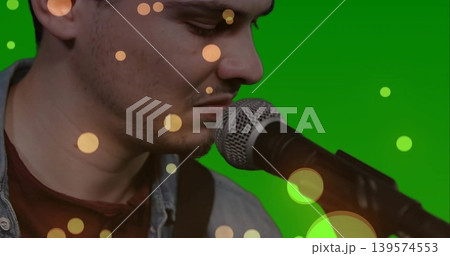 Leaning singer singing into mic stand in studio with green backdrop, denim jacket over maroon shirt Leaning singer singing into mic stand in studio with green backdrop, denim jacket over maroon shirt 139574553