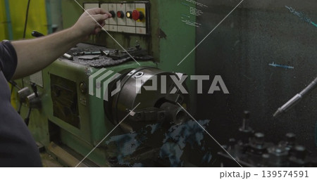 Reaching machinist in dark shirt pressing panel button on lathe in workshop with chuck, copy space 139574591