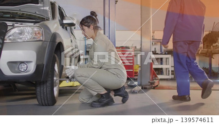 Working female mechanic in tan coveralls tightening lug nuts on silver SUV at garage 139574611