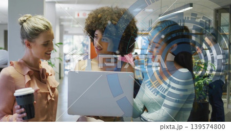 Leaning three women colleagues discussing at office, wearing tops, holding silver laptop Leaning three women colleagues discussing at office, wearing tops, holding silver laptop 139574800