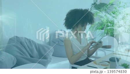 Holding tablet, woman in sleeveless white blouse focusing on screen at home desk with mug succulent Holding tablet, woman in sleeveless white blouse focusing on screen at home desk with mug succulent 139574830